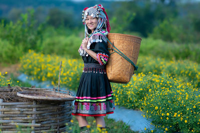 Woman holding umbrella while standing by basket on field