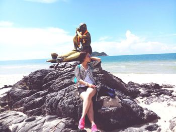 Woman on rock at beach against sky