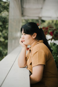 Young woman looking away while sitting on plant