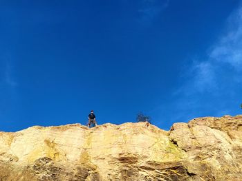 Low angle view of man on rock against blue sky