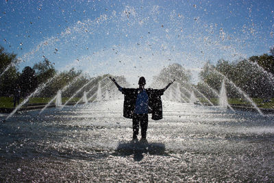 Man standing amidst fountain against sky