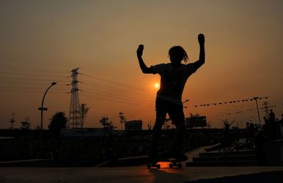 Silhouette man standing in city against sky during sunset