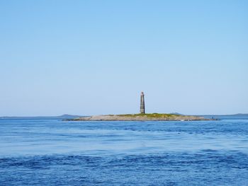 Lighthouse by sea against clear blue sky