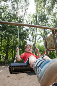 Happy boy enjoying swing in park against trees