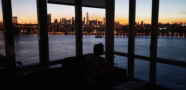 Silhouette buildings by sea against sky during sunset