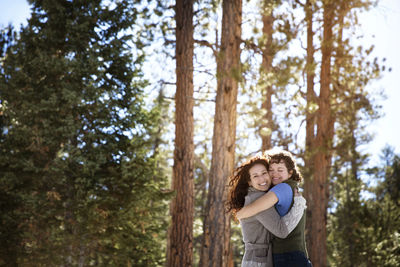 Cheerful friends hugging while standing in forest during winter