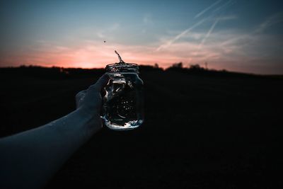 Person holding glass against sky during sunset