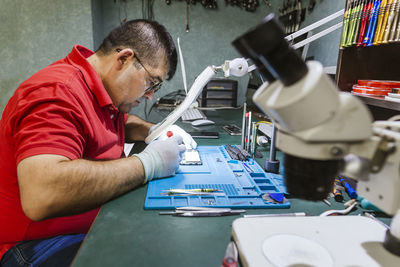 Engineer looking at broken smart phone through magnifying glass in electronics repair shop