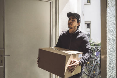 Confident delivery man with cardboard box standing at doorstep