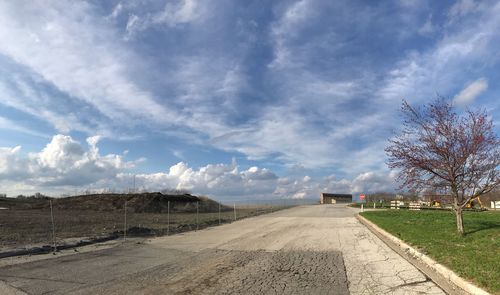 Empty road amidst field against sky