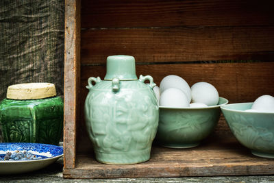 Celadon green ceramic bottle and bowls of eggs in vintage wooden box still life