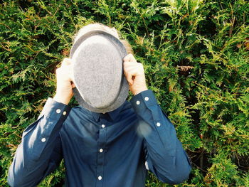 Front view of person hiding face with hat against plants