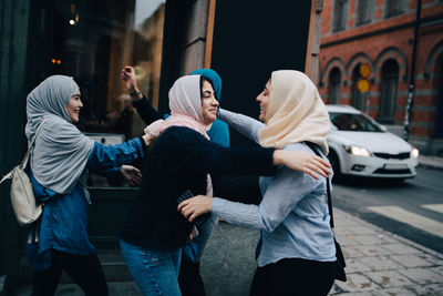 Happy multi-ethnic female friends greeting on sidewalk in city
