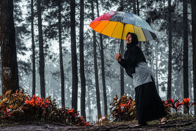 Woman with umbrella standing in forest