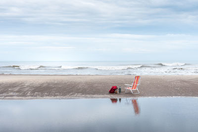 Backpack, yerba mate container and thermos next to a beach chair reflected in the water