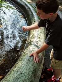 Side view of boy playing with stick in pond