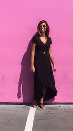 Full length of a young woman standing against pink wall