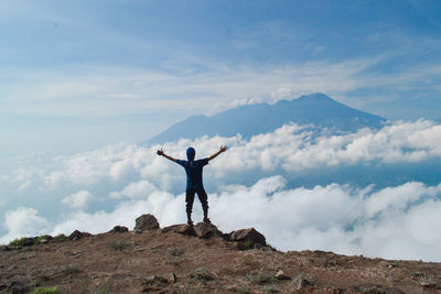 Rear view of man standing on rock against sky