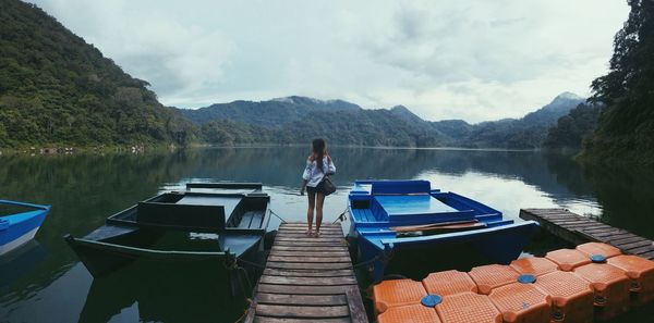 Rear view of woman standing on pier over lake against sky