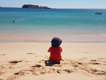 Rear view of boy on beach against clear sky