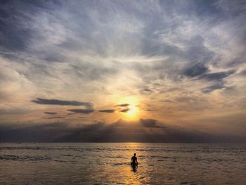 Silhouette man in sea against sky during sunset