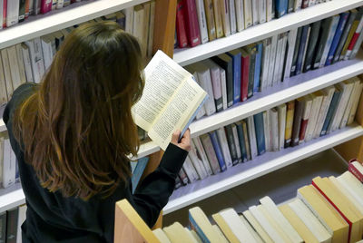 High angle view of woman reading book while standing in library