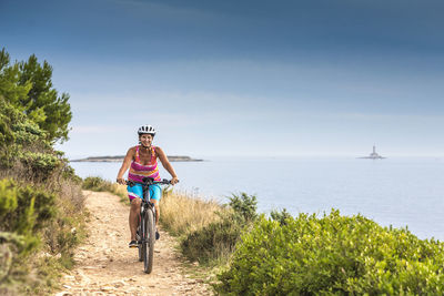 Portrait of woman riding bicycle at beach against sky