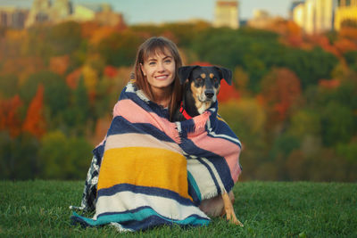 Portrait of woman with dog wrapped in shawl sitting at park