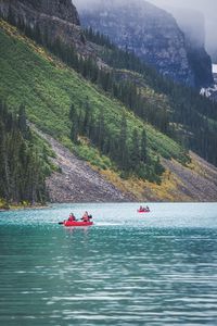 People on kayaking in river against mountains