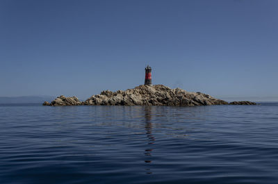 Lighthouse by sea against clear sky