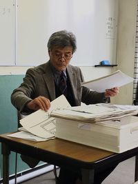 Professor with papers on desk sitting in classroom