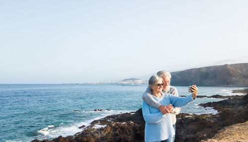 Senior couple photographing at sea against clear sky