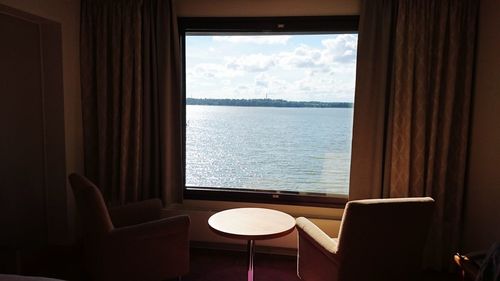 Empty chair by sea against sky seen through window