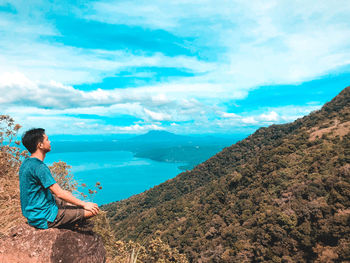 Rear view of man standing by sea against the sky while hiking in the mountain