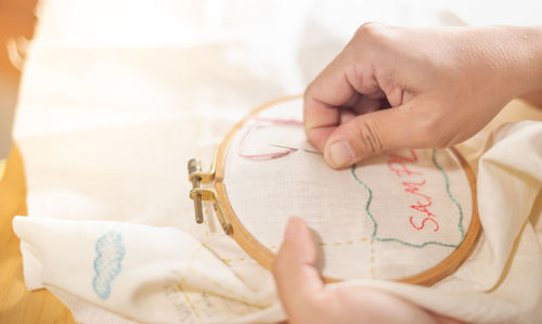 Female hand to hold wood embroidery frame and needle working on pattern stitching in a process.