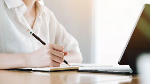 Midsection of woman using mobile phone while sitting on table