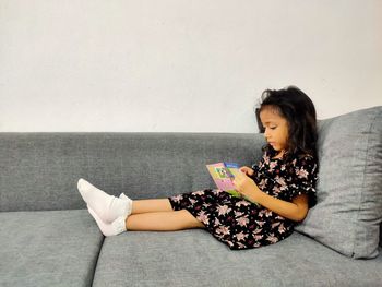 Happy girl sitting on sofa against wall