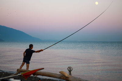 Man fishing in sea against sky