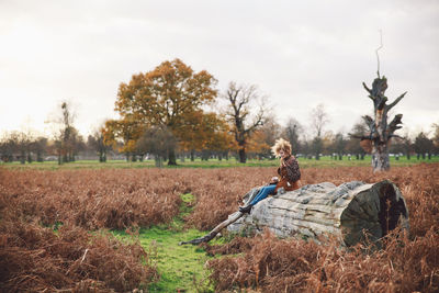 Side view of woman sitting on log at farm