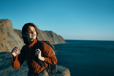 Young man standing on rock by sea against sky