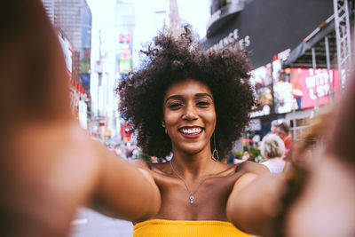 Portrait of happy young woman with afro hairstyle taking selfie on city street