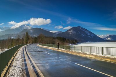 Full length of man standing on road leading towards mountains against sky