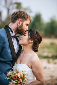 Man kissing woman on forehead against sky