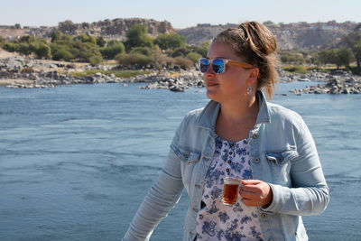 Woman in sunglasses having drink against lake