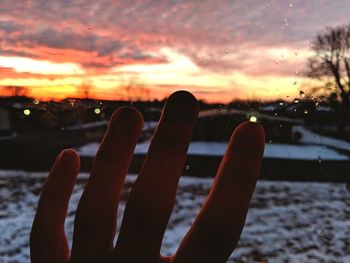 Close-up of hand against sky during sunset