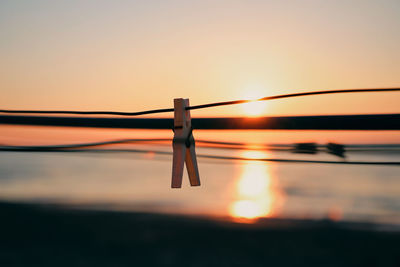 Close-up of clothespins on rope against sky during sunset