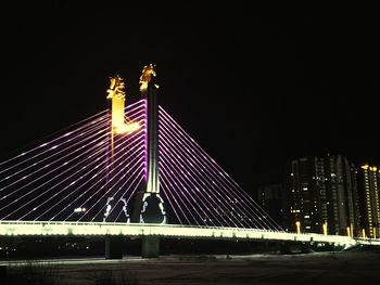 Illuminated bridge and buildings against sky at night