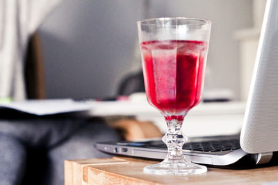 Close-up of red drink in glass by laptop on table 