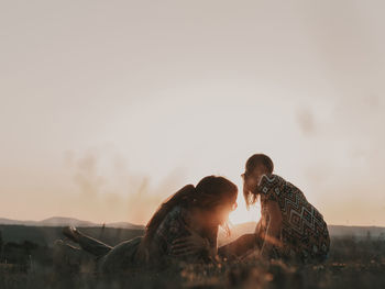 Couple of hippies with sunglasses lying on a grassy meadow in nature while watching the sunset among the mountains