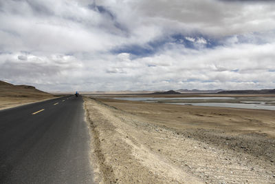 A flat newly built asphalt road calls the foot of the snowy mountain ahead